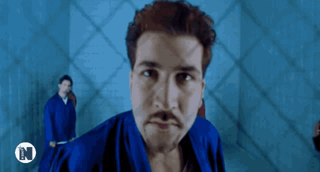 a man in a blue robe behind a chain link fence with the letter n on the bottom