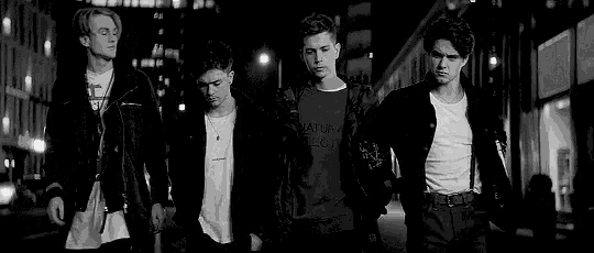 a black and white photo of a group of young men standing next to each other on a city street at night .