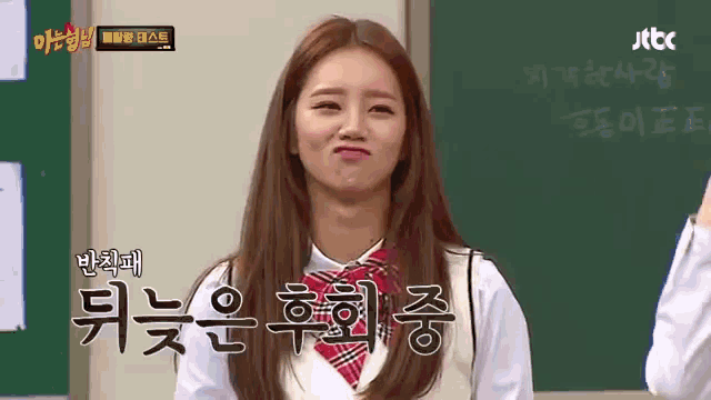 a girl in a school uniform is making a funny face in front of a chalkboard with korean writing on it .