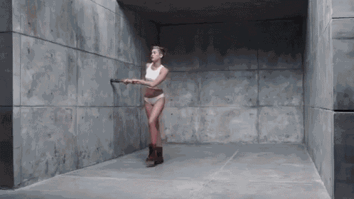 a woman in a white tank top and shorts is holding a hammer in a concrete room
