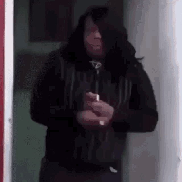 a man with long black hair is standing in a doorway holding a lighter in his hand .