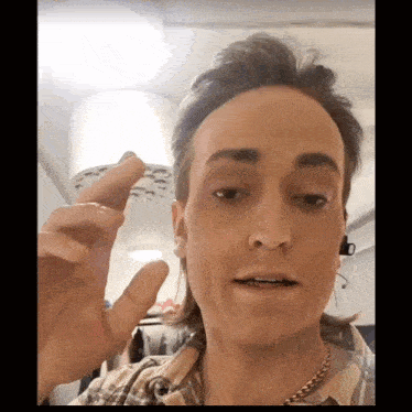 a man wearing a plaid shirt and a gold chain holds up a small object