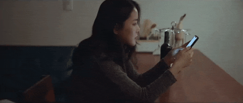 a woman is sitting at a table looking at a cell phone .