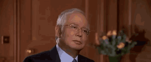 a man in a suit and tie is making a funny face while sitting in front of a vase of flowers .