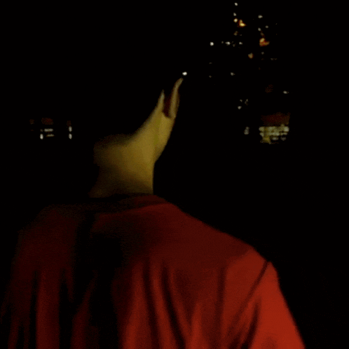 a young man in a red shirt is standing in the dark looking up