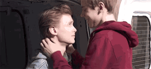 a couple of young men are standing next to each other and touching each other 's faces .