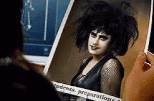 a person is holding a picture of a goth girl with students preparations written on the bottom of the picture .