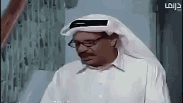 a man wearing glasses and a head scarf is standing in front of a staircase .