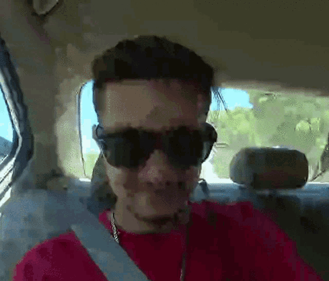 a man wearing sunglasses and a red shirt is driving a car