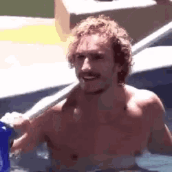 a shirtless man with curly hair and a mustache is standing in a pool .
