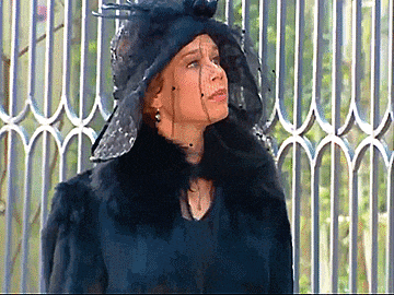 a woman wearing a black hat and fur coat is standing in front of a fence