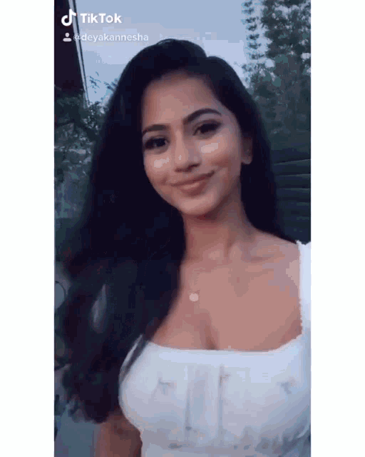 a woman with long dark hair is wearing a white top and a necklace .