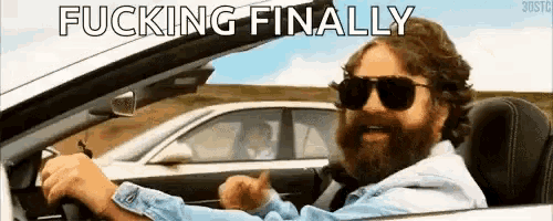 a man with a beard is driving a car with the words `` fucking finally '' written on the screen .