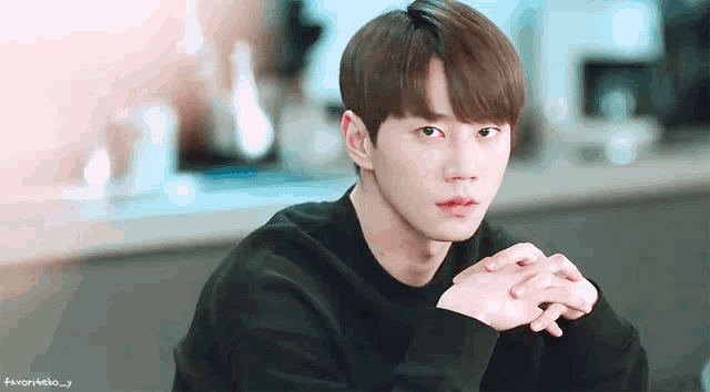 a young man in a black sweater with his hands folded