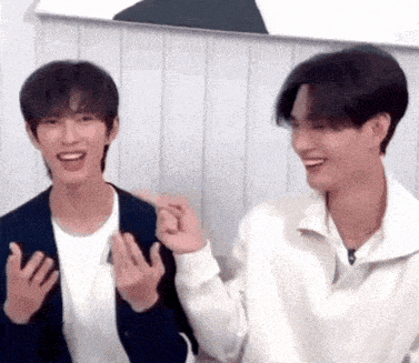 two young men are sitting next to each other and making funny faces with their hands .
