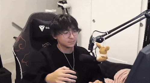 a young man is sitting in a chair holding a stuffed animal and looking at a computer screen .