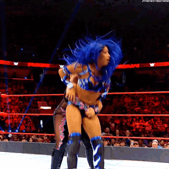 a woman with blue hair is holding another woman in a wrestling ring