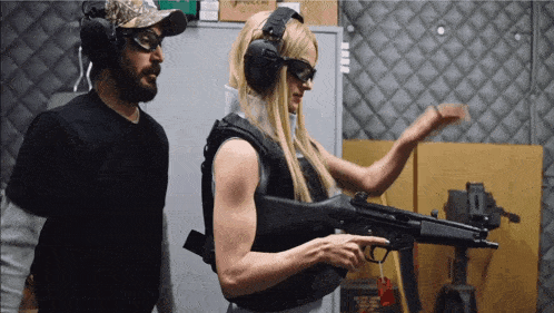 a man stands next to a woman holding a gun in a room