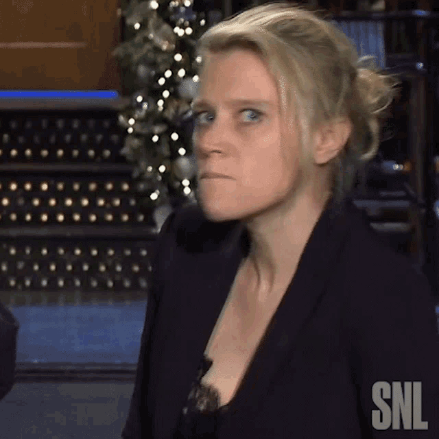 a woman is making a funny face in front of a christmas tree and a sign that says snl