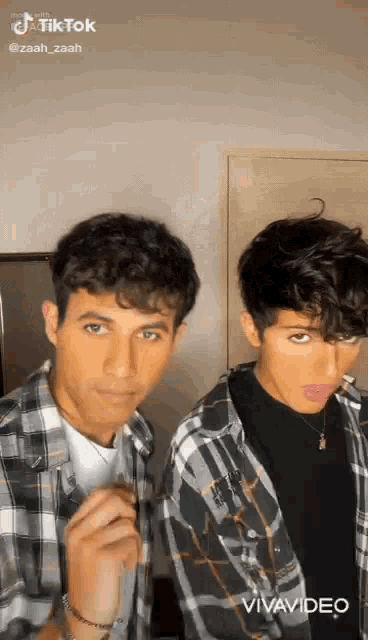 two young men are standing next to each other in a room and making funny faces .