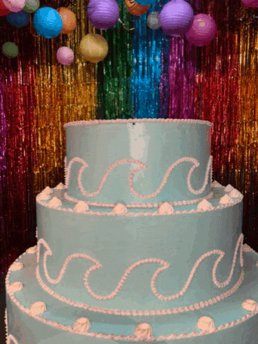 a blue cake with pink waves on it in front of a rainbow curtain