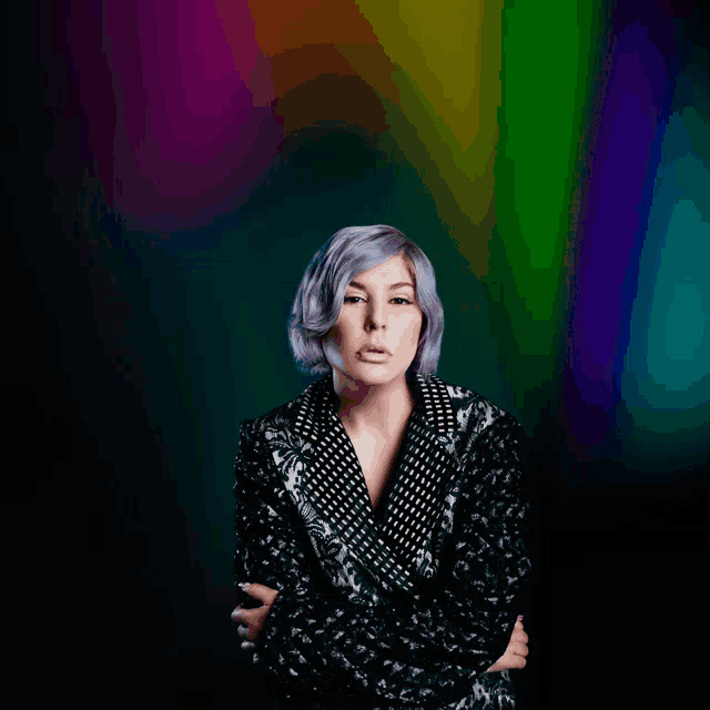 a woman with purple hair is standing in front of a rainbow colored background