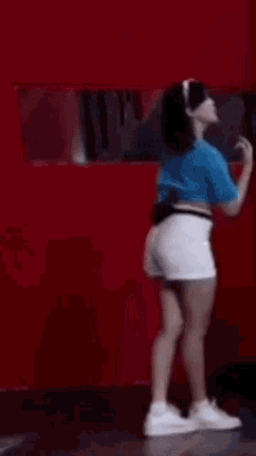 a woman in a blue crop top and white shorts is making a heart with her hands .