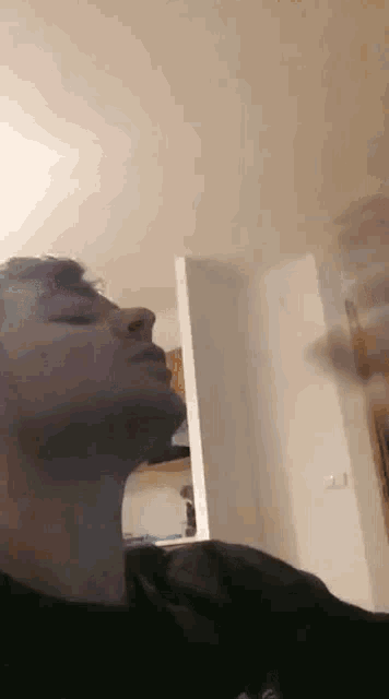 a man is smoking a cigarette in a room with his eyes closed and a smoke coming out of his mouth .