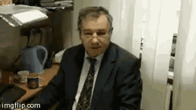 a man in a suit and tie is sitting at a desk with a computer .