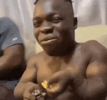 a shirtless man is sitting on a couch eating french fries .