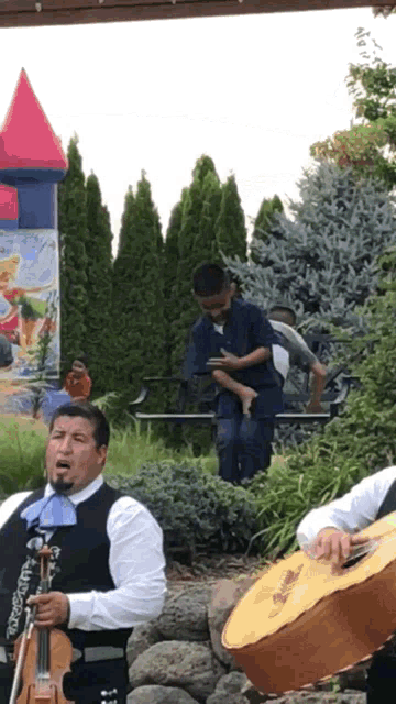 a man playing a guitar and another man playing a violin in front of a bouncy house