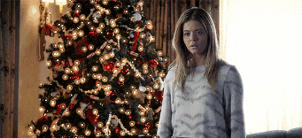 a woman stands in front of a christmas tree