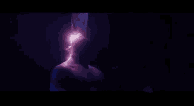 a person is standing in a dark room with a purple light coming from their chest .
