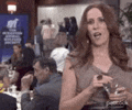 a woman is standing in front of a crowd of people in a restaurant holding a glass of wine .