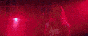 a woman in a white dress is standing in front of a crowd in a dark room surrounded by purple lights .