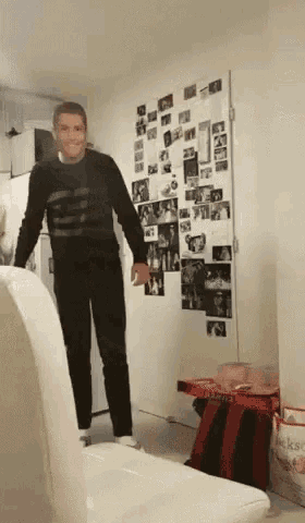 a man in a black sweater is standing in front of a wall full of pictures