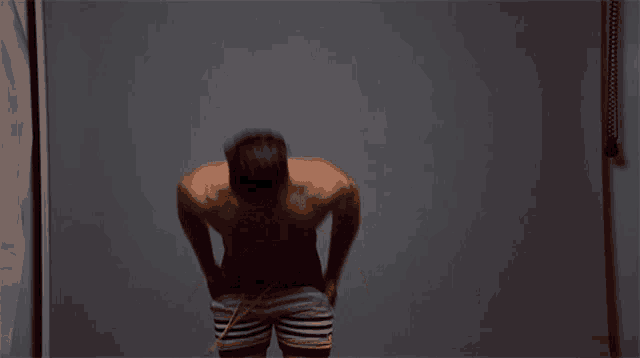 a shirtless man in striped shorts is measuring his waist