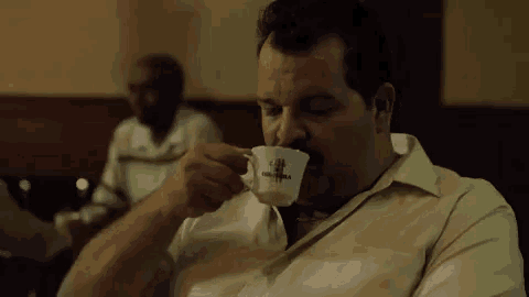 a man is drinking a cup of coffee in a restaurant while sitting at a table .