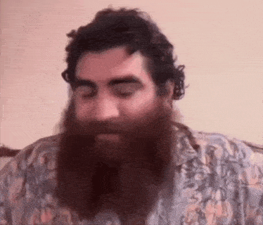 a man with a long beard and curly hair is sitting on a couch .