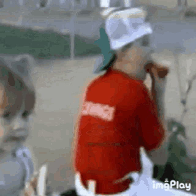a boy in a red shirt is eating a hot dog while another boy watches .