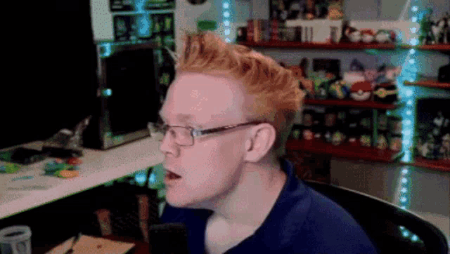 a man with red hair and glasses sits in front of a computer