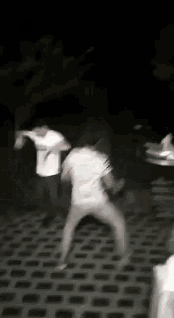 a group of men are fighting each other on a brick sidewalk at night .