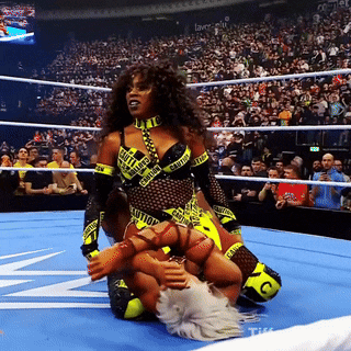 a woman in a caution tape outfit is kneeling on another woman in a wrestling ring