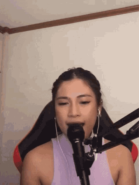 a woman in a purple tank top is singing into a microphone while wearing headphones .