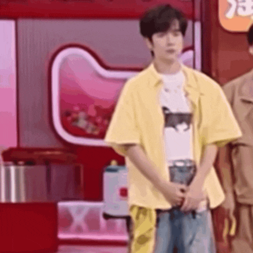 a man in a yellow shirt and jeans is standing in front of a red wall holding a microphone .