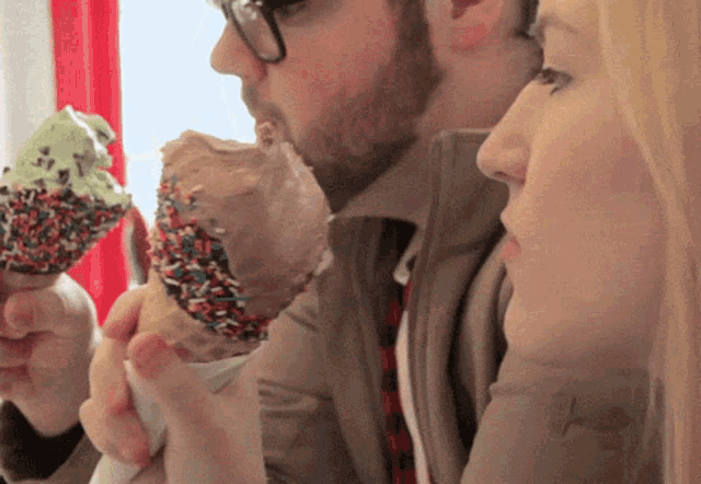 a man and a woman are eating ice cream cones with sprinkles on them