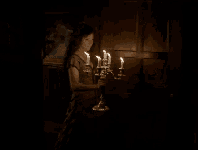 a woman in a dark room holding a candelabra with candles on it