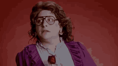 a man wearing glasses and a purple dress is holding a red rose .