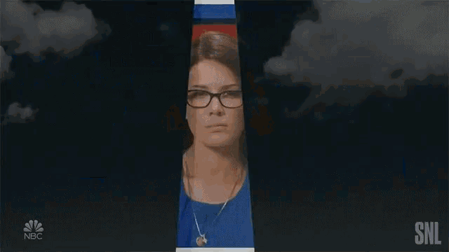 a woman wearing glasses and a blue shirt is standing in front of a nbc logo