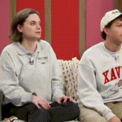 a man and a woman are sitting on a couch and the woman is wearing a xavier shirt
